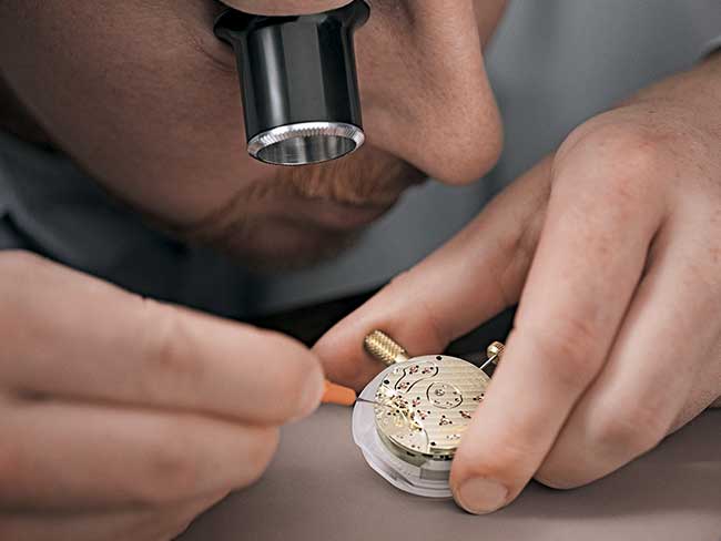 Uhrmacher überprüft Einzelteile und Funktion eines Uhrwerks